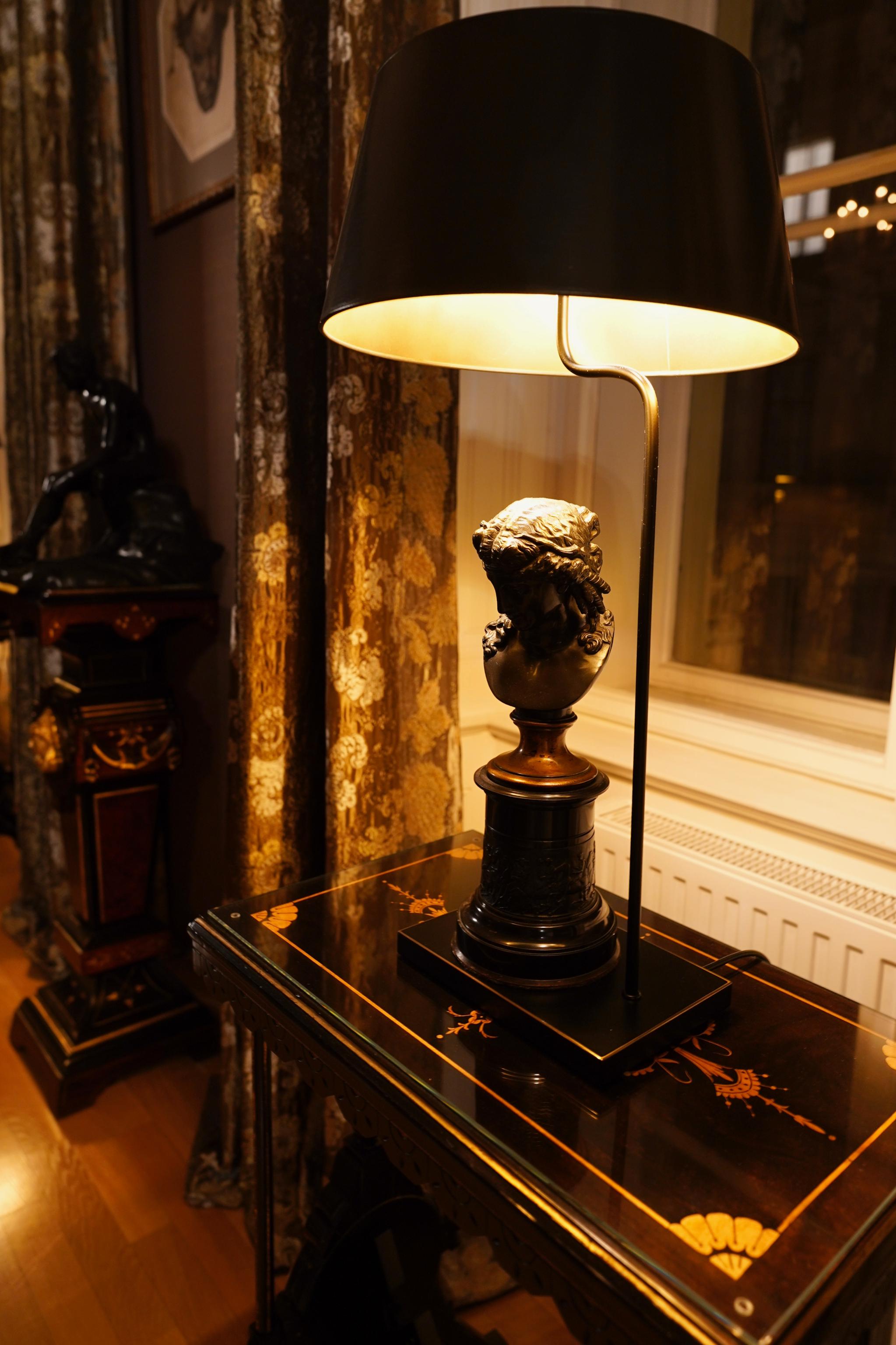 Salonische Lampe und klassische Büste auf dunklem Tisch.